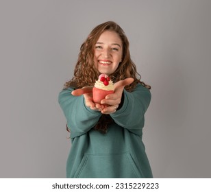 A cute girl is holding a cake-candle. Red-haired happy girl on a gray background - Shutterstock ID 2315229223