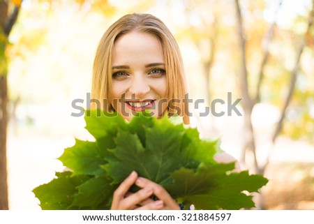 Cute Girl holding in hands green maple leaves Young adult woman wear colorful dress with flowers pattern Female stand outdoor against yellow autumn park Empty copy space for inscription 