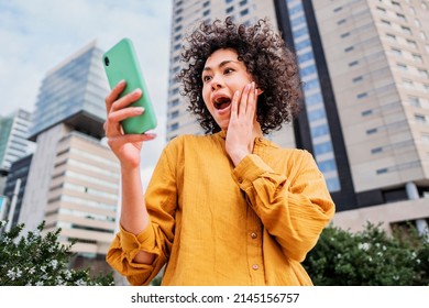 Cute girl holding smart phone in hand, surprised young woman watching cell