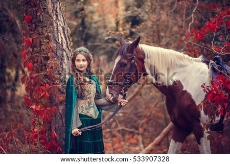Cute girl in the hooded cloak with a horse in autumn forest. Fairy elf.