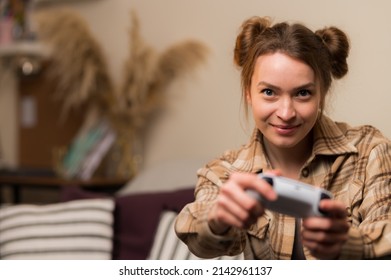 A cute girl with a joystick plays a video game at home in the room. Interesting entertainment, gaming, communication, online games with friends, win, win, game strategy.