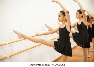 Cute Girl In A Leotard And Skirt Lifting Her Leg And Arm During A Ballet Dance Class