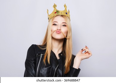 Cute girl with light brown hair and nude make up wearing jacket and crown on head, making funny pose at gray studio background.