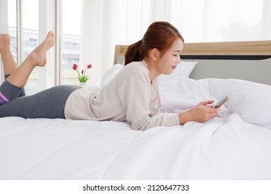 Cute girl lying on a white bed playing smart phone With a bright and happy smile. - Shutterstock ID 2120647733