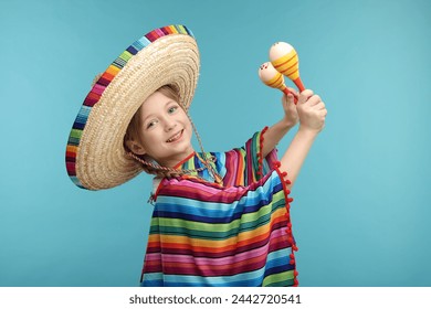 Cute girl in Mexican sombrero hat and poncho dancing with maracas on light blue background - Powered by Shutterstock