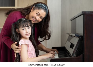 Cute Girl And Mother Playing The Piano Together In Living Room At Home. Asian Pianist Teacher Teaching Little Girl Kid Student To Play Piano At School.