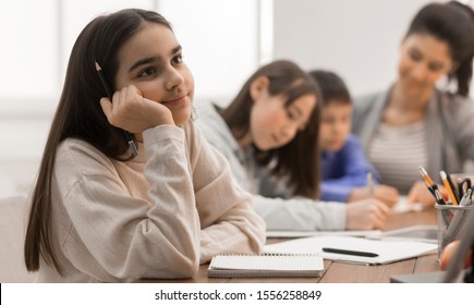 Cute Girl Not Paying Attention In Classroom At The Elementary School, Teacher And Classmates On Background