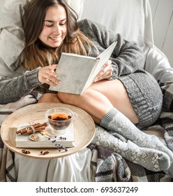 Cute girl on a comfortable chair with tea ,reading a book, the concept of comfort and hipster