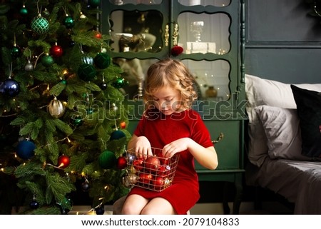 cute girl playing with Christmas decoration near Christmas tree indoors. Merry Christmas and Happy Holidays