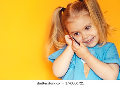  cute girl with ponytails uses a smartphone, smiling toddler, on an orange background, close-up, telephone conversation, telephone connection