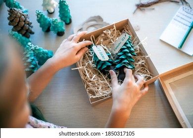 Cute Girl Preparing DIY Gifts And Signing Tags To Parents And Family For Christmas, A Green Cone As If It Is Small Toy Pine Tree, Tags And Festive Boxes, Handmade Presents, Zero Waste Holidays