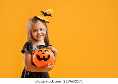 Chica linda con cubo de calabaza vestida como bruja sobre fondo amarillo, espacio para texto. Halloween celebración