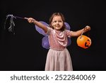 Cute girl with pumpkin bucket and magic wand dressed like fairy for Halloween celebration on black background