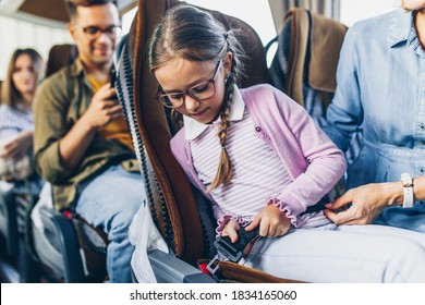 Cute girl putting on seat belt and traveling in bus with mother.