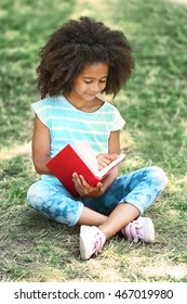Cute girl reading book on green grass