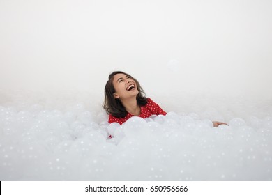 A cute girl with red polka dot t-shirt among the lots of white ball in Ball pit. She feel happy and enjoy with childhood moments. (with copy space)
