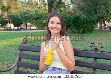 Cute girl is relaxing in the park and drinking cool juice in a hot day.
