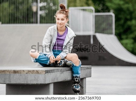 Cute girl roller skater sitting in city park and smiling. Pretty female teenager posing during rollerskating