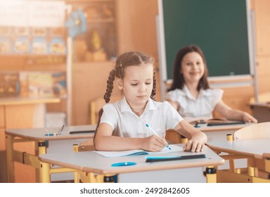 A cute girl sits in a classroom at a table with notebooks and textbooks. The student writes in a notebook. Back to school. School supplies. Student at a lesson, class during a lesson.
 - Powered by Shutterstock