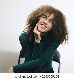 A Cute Girl Is Sitting On A Chair, Wearing A Green T-shirt And Looking To The Side. Sensual Fresh Happy Face, Positive Emotions.Watching To The Left At Copy Space, Closeup.Lifestyle, People Concept. 