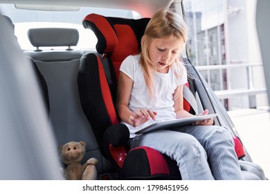 Cute Girl Is Sitting In Safe Child Seat And Using Tablet And Internet On Road