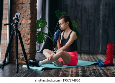 Cute Girl In Sportswear Sits Sideways On A Yoga Mat In Front Of The Camera And Drinks Water From A Bottle While Holding It In Her Hand