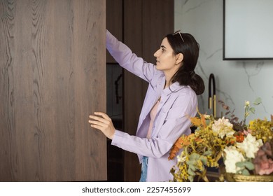 A cute girl is standing in the kitchen with an open cupboard and takes out groceries. - Shutterstock ID 2257455699