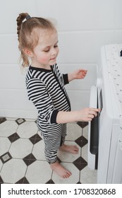 Cute girl in striped clothes turns on the washing machine. Cleanliness and Household Concept