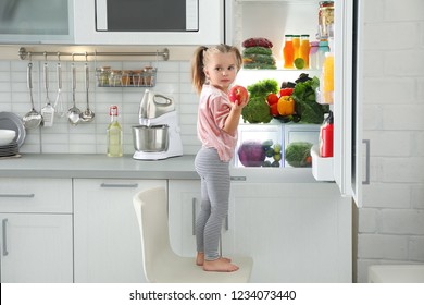 Cute Girl, das Apfel aus dem Kühlschrank in der Küche holt