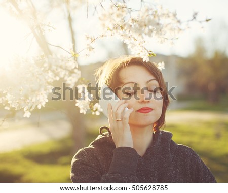Cute girl talking on cell phone. Portrait of a close-up on the background of cherry blossoms and the setting sun.