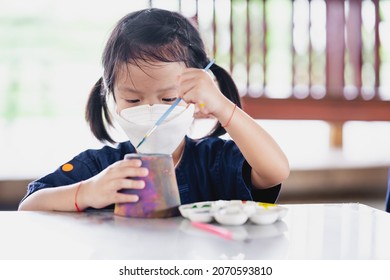 Cute girl is using her left hand to paint watercolor on pottery. Children wear white face mask to prevent spread coronavirus and PM 2.5 air pollution. - Powered by Shutterstock