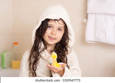 Cute girl wearing a bathrobe with wet hair after bath or shower, laughing and smiling. Bathroom at home. 