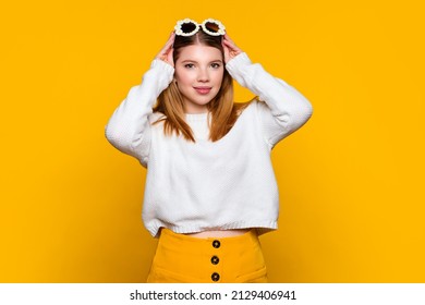 Cute girl wears casual outfit and stylish daisies sunglasses looking at camera and smile. Young woman wait oncoming of spring on yellow background. Lifestyle. Trendy accessory