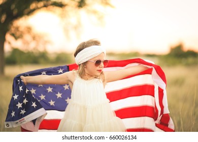 Cute Girl In White Headband And Dress Holds Up American Flag In A Field