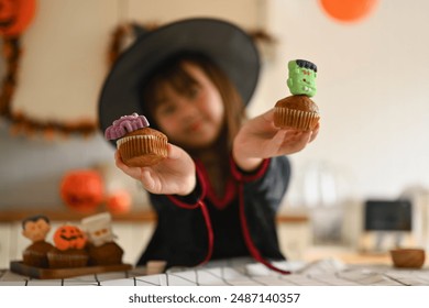 Cute girl in witch costumes holding delicious Halloween cupcakes. Select focus on hand - Powered by Shutterstock