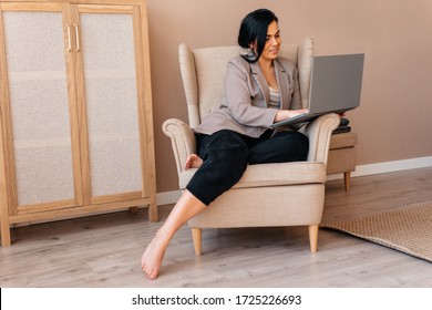 Cute girl working with her laptop sitting in the armchair at home