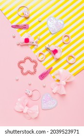 Cute Girl's Hair Accsessories On Pink And Yellow Striped Background. Hair Clips, Hairpins, Bow Tie On Pink Background. Fashion Hair Accessories For Little Girls. Flat Lay. Place For Text.