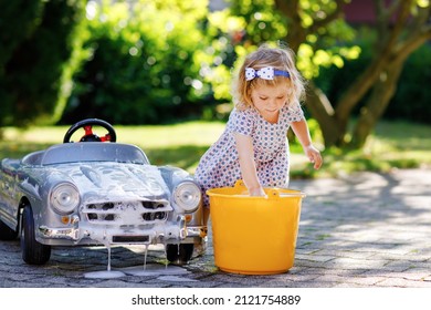 Cute Gorgeous Toddler Girl Washing Big Old Toy Car In Summer Garden, Outdoors. Happy Healthy Little Child Cleaning Car With Soap And Water, Having Fun With Splashing And Playing With Sponge.