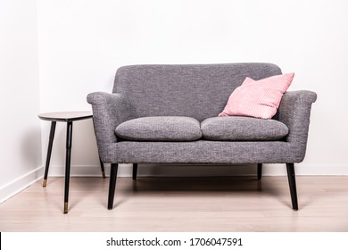 A cute gray settee with a pink pillow sitting on it, next to a small, contemporary occasional table.  - Shutterstock ID 1706047591