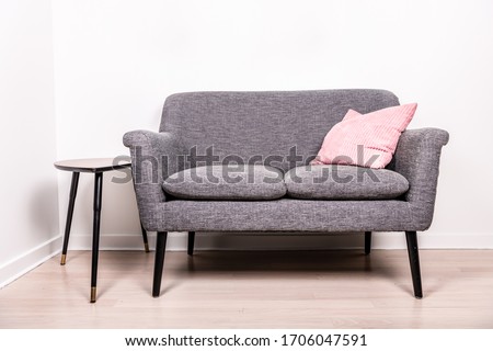 A cute gray settee with a pink pillow sitting on it, next to a small, contemporary occasional table. 