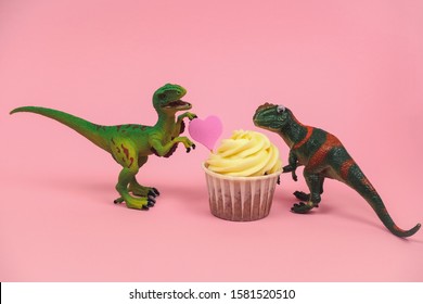 Cute Green Plastic Dinosaur Toys With Cupcakes Decorated With Pink Heart On A Pastel Pink Background 