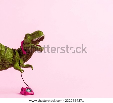 Cute green toy dinosaur speaking on retro phone on pink background. Copy space. 
