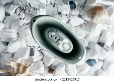 Cute Grey Small Silicone Toy Boat With Holes On Top Floating On Surface Of Water Above Bottom With White Stones And Shell. Transparent Fresh Water With Flecks And Waves. Top View. Baby Toy, Water Game