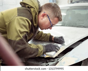 Cute Guy In Black Glasses With Black Gloves Displays The Shape Of The Hood For The Subsequent Painting Of The Car. Guy - A House Painter Working On A Car In The Garage