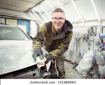 Cute Guy In Black Glasses With Black Gloves Displays The Shape Of The Hood For The Subsequent Painting Of The Car. Guy - A House Painter Working On A Car In The Garage