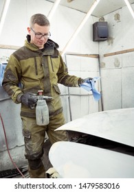 Cute Guy In Black Glasses With Black Gloves Displays The Shape Of The Hood For The Subsequent Painting Of The Car. Guy - A House Painter Working On A Car In The Garage