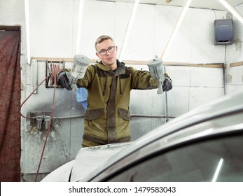 Cute Guy In Black Glasses With Black Gloves Displays The Shape Of The Hood For The Subsequent Painting Of The Car. Guy - A House Painter Working On A Car In The Garage