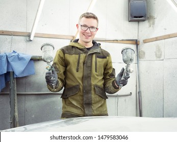 Cute Guy In Black Glasses With Black Gloves Displays The Shape Of The Hood For The Subsequent Painting Of The Car. Guy - A House Painter Working On A Car In The Garage