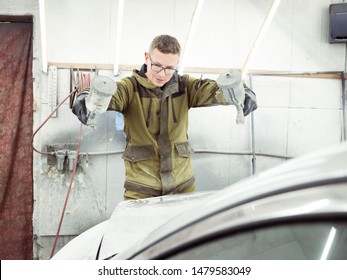 Cute Guy In Black Glasses With Black Gloves Displays The Shape Of The Hood For The Subsequent Painting Of The Car. Guy - A House Painter Working On A Car In The Garage