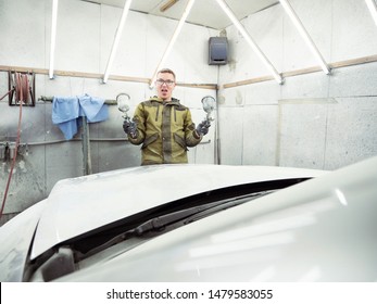 Cute Guy In Black Glasses With Black Gloves Displays The Shape Of The Hood For The Subsequent Painting Of The Car. Guy - A House Painter Working On A Car In The Garage